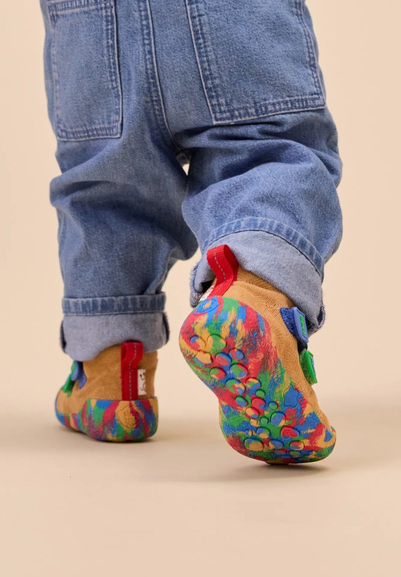 Bunte Kinderschuhe mit einer strukturierten Sohle, die eine Mischung aus roten, blauen und grünen Akzenten aufweisen. Hergestellt aus weichem, hellbraunem Material mit lebhaften Mustern.