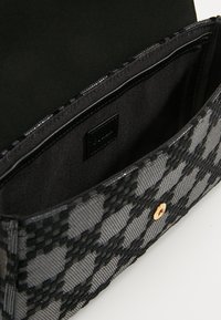 Czarna torebka o plecionej fakturze z kratkowanym wzorem, złotym zamknięciem zatrzaskowym oraz czarnym materiałowym wnętrzem z miejscami na karty.