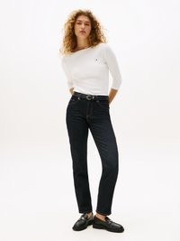 Weißes Langarmhemd mit rundem Ausschnitt, kombiniert mit dunkelblauen Jeans und schwarzen Slippern. Schlichtes, tailliertes Design mit minimalen Details.