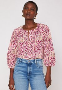 Blusa a fiori rosa e bianca con maniche a tre quarti, scollatura rotonda e patta frontale. Abbinata a jeans blu a vita alta.