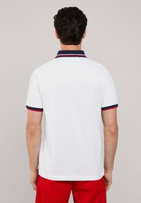 Camisa polo blanca con cuello azul marino y acentos a rayas rojas y azul marino en las mangas. Tejido de algodón suave, mangas cortas y corte estándar.