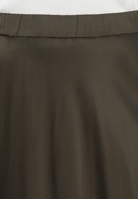 Tumši brūna svārku ar gludu, nedaudz spīdīgu tekstūru. Elastīga jostasvieta ar smalku krokām augšpusē, nav redzamu aizdaru vai rakstu.