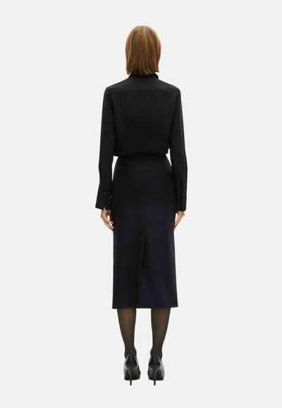 Blusa nera con colletto e maniche lunghe, abbinata a una gonna blu scuro fitted con uno spacco posteriore, indossata con scarpe nere con tacco.