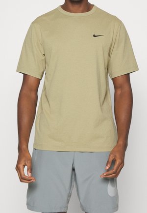 T-shirt en coton vert olive avec des manches courtes, col rond et un petit logo Nike noir sur la poitrine à gauche. Associé à un short gris clair.