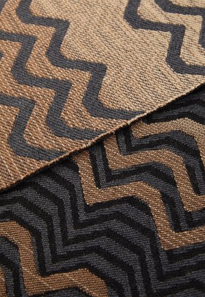 Tekstil med zigzag-mønstre i jordtoner af brunt og sort; har en tekstureret overflade og markante kontrasterende design.