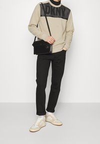 Felpa beige con logo DKNY, dettagli neri, pantaloni neri, sneakers beige e bianche, e una borsa a tracolla nera. Tessuto morbido, vestibilità casual.