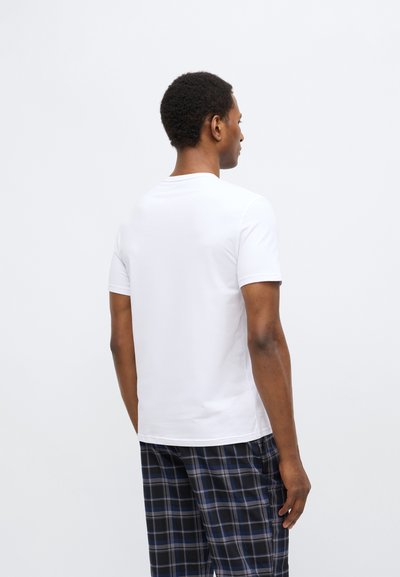 Balta īsroku t-krekls ar apaļu kakla izgriezumu un gludu tekstūru. Valdāts ar melnām un zilām pledveida pidžamas biksēm, attēlots no muguras.