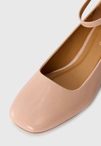 Light pink patent leather ballet flat with a square toe and an ankle strap. Smooth surface, minimal stitching detail.