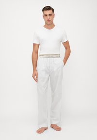 Witte T-shirt en lichtgrijze gestreepte broek met elastische Calvin Klein tailleband, die een ontspannen pasvorm en lichtgewicht stof benadrukken.