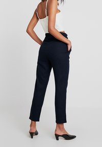 Námořnické kalhoty s tapered střihem, vyrobené z lehké látky. Obsahují boční kapsy a vysoký pas, doplněné černými muly.