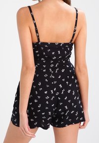 Svart jumpsuit med tunna band, med ett blommönster i vitt. Strukturerad bodice med rynkdetaljer, löst sittande shorts.