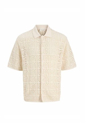 Chemise beige en crochet à manches courtes avec un col pointu et une fermeture boutonnée sur le devant, présentant un motif à tissage ouvert en forme de grille.