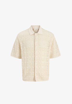 Chemise beige en crochet à manches courtes avec un col pointu et une fermeture boutonnée sur le devant, présentant un motif à tissage ouvert en forme de grille.