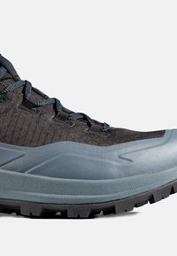 Sort og grå vandresko med tekstureret stofoverdel, tyk beskyttende tåhætte, mønstrede snørebånd og robust sål med slidbane på hvid baggrund.