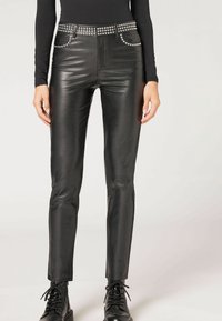 Svarta läderbyxor med slimmad passform, som har silverfärgade nitar längs midjan och framfickorna. Slät textur och rak bendesign.