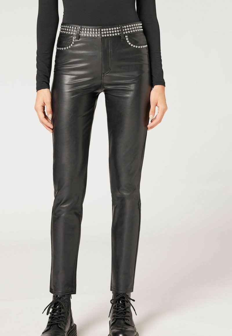 Svarta läderbyxor med slimmad passform, som har silverfärgade nitar längs midjan och framfickorna. Slät textur och rak bendesign.