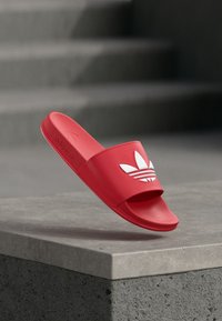 Rød gummisandale med åpen tå og bred stropp med hvit Adidas-logo og tre striper. Teksturert fotseng for godt grep.