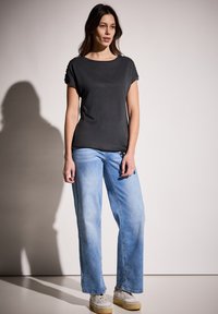 Černá krátkosrstá košile s kulatým výstřihem, spárovaná se světle modrými širokými džíny a bílými teniskami. Jednoduchý design a volný střih.