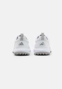 White athletic shoes with a textured mesh upper, grey accents, and a rubber sole featuring traction spikes. Minimalist design, pull tab on heel.