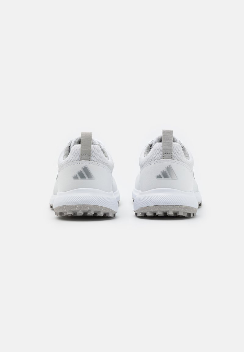 Weiße Sportschuhe mit einem strukturierten Mesh-Obermaterial, grauen Akzenten und einer Gummisohle mit Traktionsspikes. Minimalistisches Design, mit Zuglasche an der Ferse.