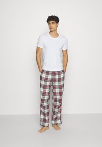 Weißes T-Shirt mit kurzen Ärmeln und karierten Schlafanzughosen in Rot, Marineblau und Weiß. Der Stoff ist weich und die Hose hat eine lockere Passform.