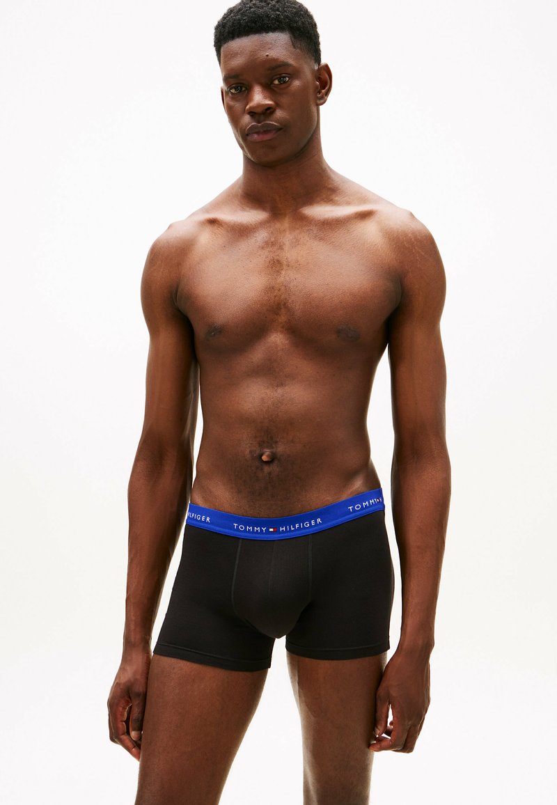 Boxers noirs avec une ceinture bleu présentant le logo "TOMMY HILFIGER". Texture de tissu lisse, design ajusté, longueur mi-cuisse.