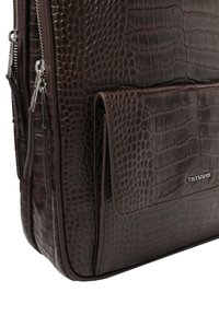 Brązowa torba ze skóry o fakturze z wzorem skóry krokodyla; wyposażona w srebrne okucia oraz przednią kieszeń z metalowym logo.