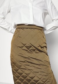Gep quilteter, olivgrüner Bleistiftrock mit glatter Textur und figurbetontem Design. Verfügt über einen Taillengummi und eine Rautensteppung.