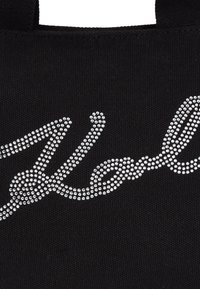 Dettaglio di una borsa nera in tessuto con il logo "YSL" formato da piccoli strass argentati in un design corsivo.