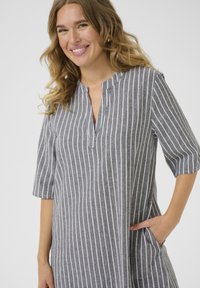 Robe grise avec des rayures verticales blanches, manches courtes, décolleté en V et poches avant. Texture douce, design décontracté adapté à diverses occasions.