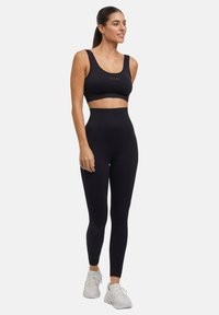 Zwarte sportcrop top en hoge taille leggings, gemaakt van rekbare stof. Bevat minimale rode accenten aan de zijkant van de leggings.