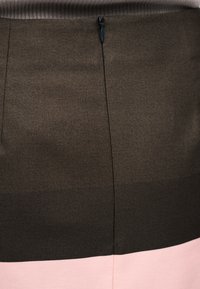 Κοντινή λήψη ενός ενδύματος που δείχνει μια καφέ ύφανση με μια μαύρη φερμουάρ πάνω από μια ανοιχτό ροζ υφασμάτινη λωρίδα.