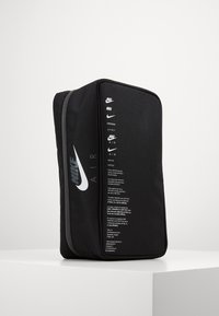 Svart rektangulär Nike Air-väska med vita logotyper och text, stående upprätt på en vit yta mot en enfärgad bakgrund.