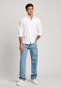 Witte lange mouwen knoopshirt, lichtblauwe spijkerbroek en witte sneakers. Het shirt heeft een kraag en is gemaakt van lichtgewicht stof.