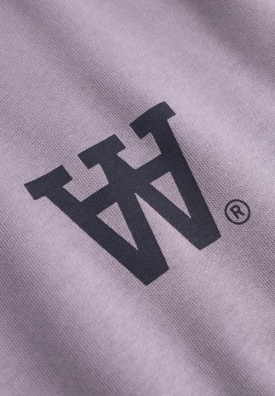 Un tissu violet à finition texturée présente un logo noir bien visible incorporant les lettres « W » et « H », accompagné d'un symbole de marque déposée.