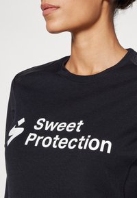 Must mustripu seljasärk, millel on valge "Sweet Protection" logo, ümmargune kaelus ja tekstuuriga aktsendid õlgadel.