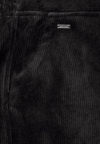 Černá kordurová látka s vertikálními proužky a malou metalickou nálepkou s textem "StreetOne." Měkká textura a teplý vzhled.