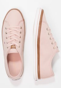 Paire de baskets basses rose clair avec semelles blanches et garniture marron, avec lacets et œillets en métal, vues de dessus et de côté.