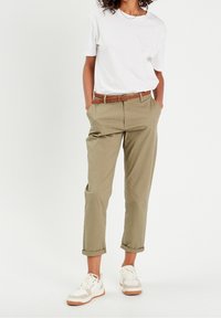 Pantalon en coton beige avec une coupe décontractée, ourlets roulés et une ceinture tressée marron. Assorti à un t-shirt blanc et des baskets blanches avec des accents beiges.