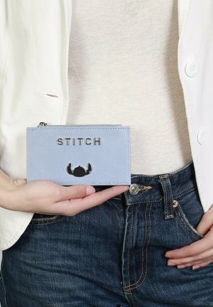 Porte-cartes en cuir bleu clair avec des lettres "STITCH" argentées et des détails en noir. Fermeture zippée ; forme rectangulaire.