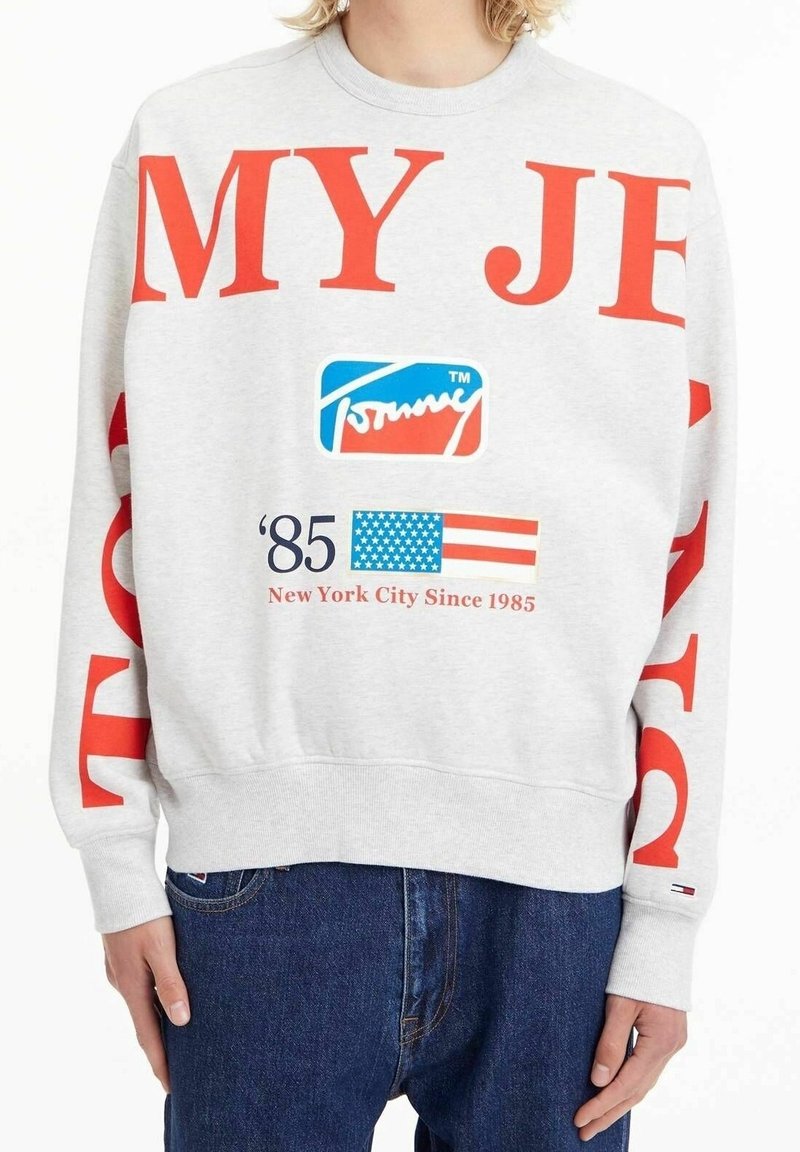 Grå sweatshirt med röd text, som har en logotyp och en grafisk flagga. Avslappnad passform med ribbade ärmslut och nederkant.