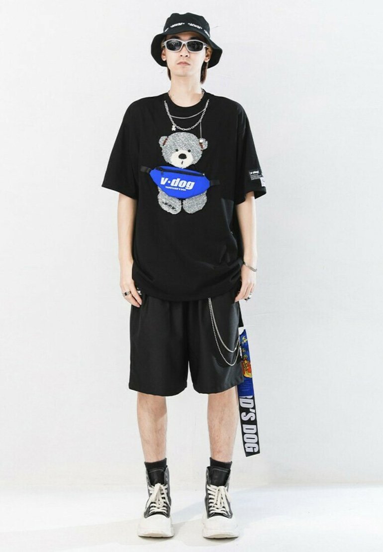 T-shirt negra de gran tamaño con un gráfico de oso, combinada con pantalones cortos negros y zapatillas altas. Incluye una riñonera azul y gafas de sol.