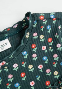 Zielony prążkowany materiał z kolorowym kwiatowym wzorem, w którym znajdują się czerwone, różowe, żółte i niebieskie kwiaty, z falbaniastym dekoltem i widoczną metką z instrukcjami pielęgnacji.