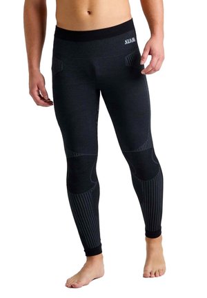 Vista recortada de una persona que lleva unos leggings negros de compresión con paneles acanalados y está descalza sobre un fondo blanco.