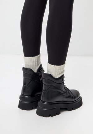 Sorte ankelstøvler i læder med robust sål, snørelukning og lynlåsdetalje. Båret med cremefarvede ribstrikkede sokker og sorte leggings.