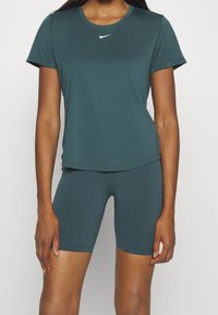 Camiseta atlética de Nike en color verde azulado con mangas cortas y escote redondo, combinada con mallas de ciclismo a juego en el mismo tono. Tejido suave y elástico.