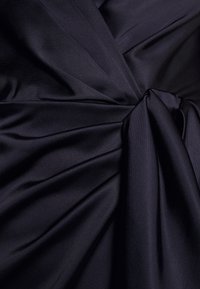 Dark navy fabric with a smooth texture, featuring pleats and a knotted accent at the center, highlighting a structured design.