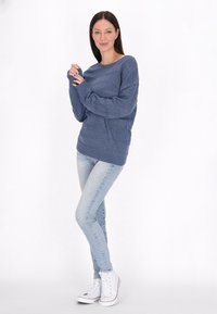 Kék kötött pulóver vízszintes bordázott mintákkal, hosszú ujjakkal és laza fazonnal, világoskék skinny farmernadrággal és fehér sportcipővel párosítva.