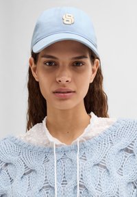Lys blå baseballcap med brodert bokstav "S" i off-white. Capen har en buet skjerm og er laget av teksturert bomullsstoff.