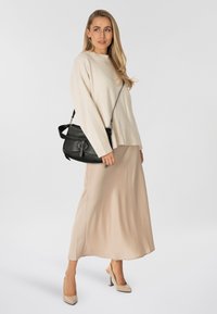 Beige gebreide trui met geribbelde zoom, gecombineerd met een vloeiende beige rok. Zwarte leren crossbodytas met een ronde gesp als detail.